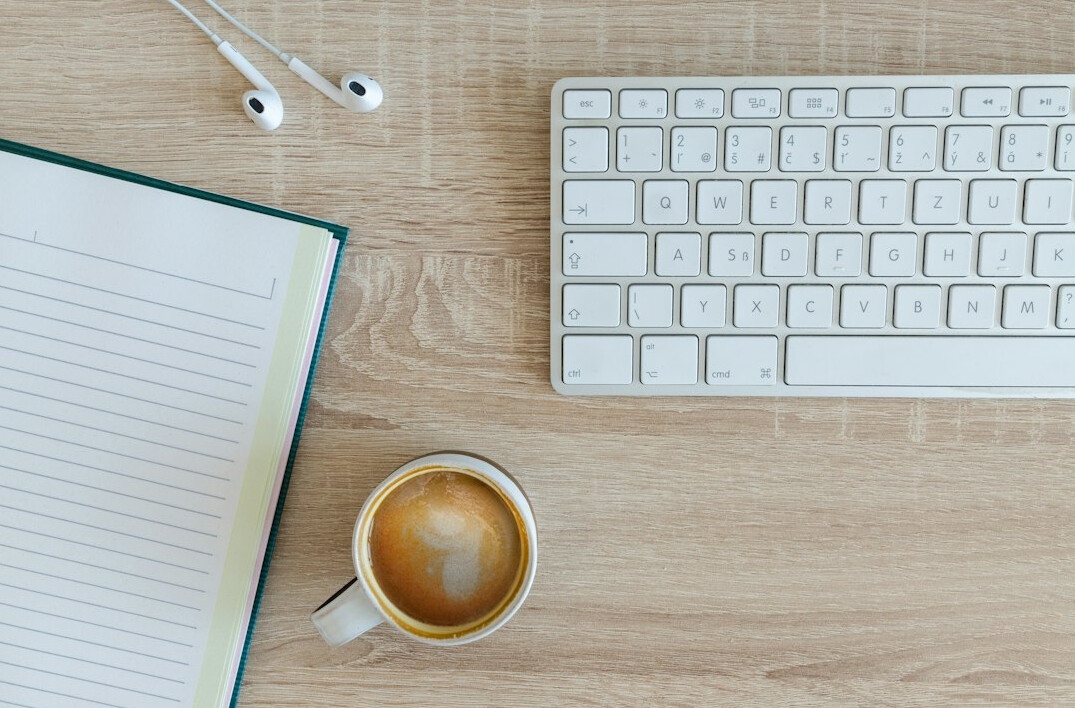 Hands typing on a laptop keyboard with a notebook beside it